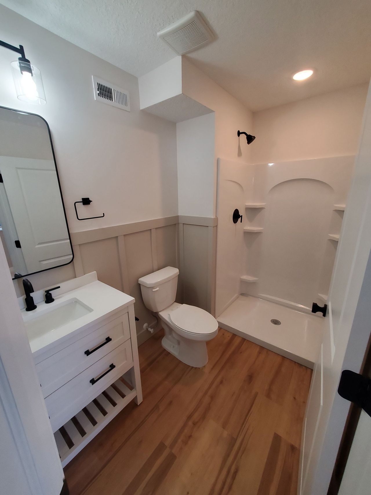 Small bathroom with white vanity, toilet, walk-in shower, and wood-look floor.
