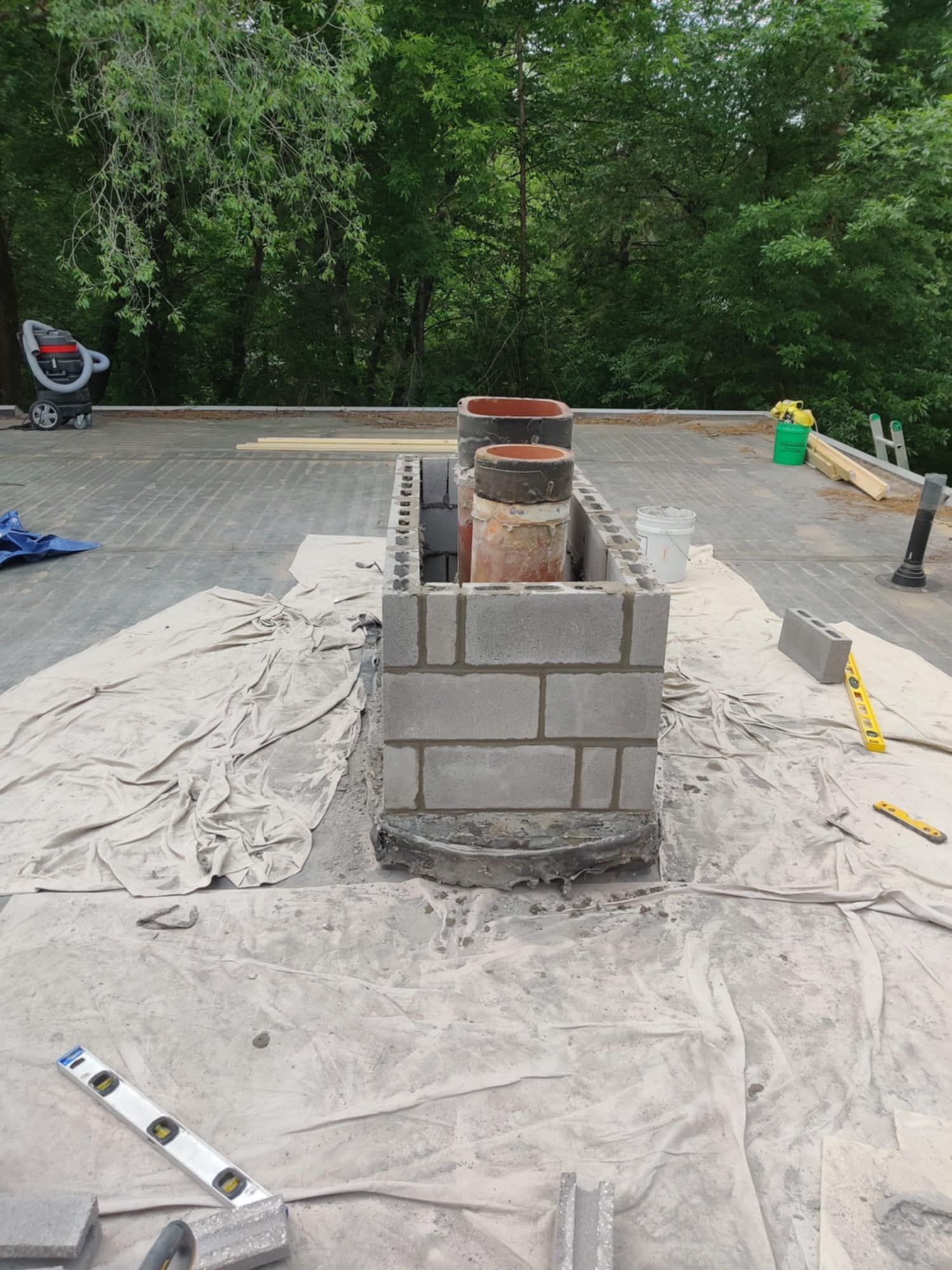 Partially built brick structure with a metal pipe on a tarp-covered outdoor worksite