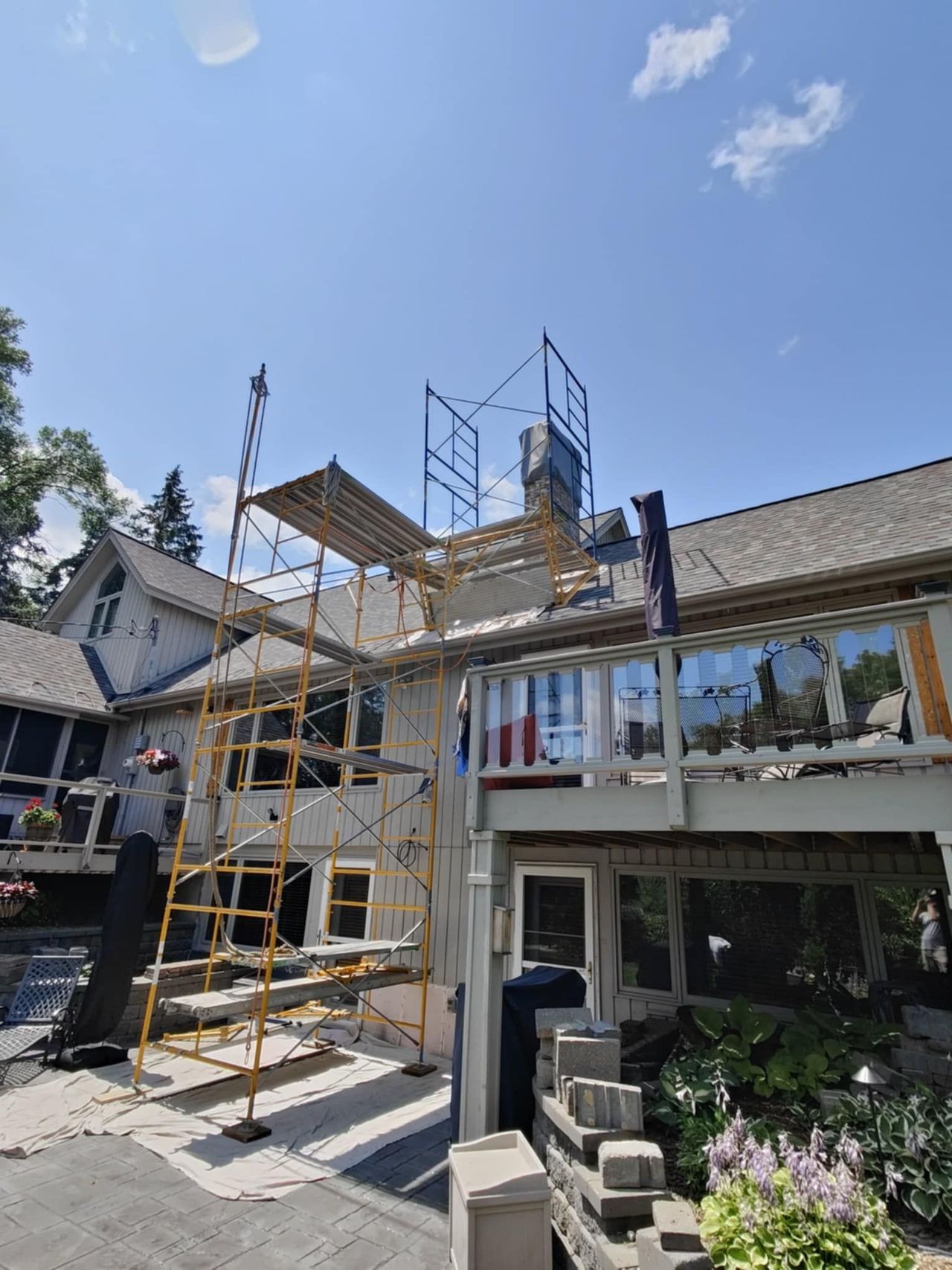 Scaffolding beside a house with workers repairing the roof under a clear blue sky