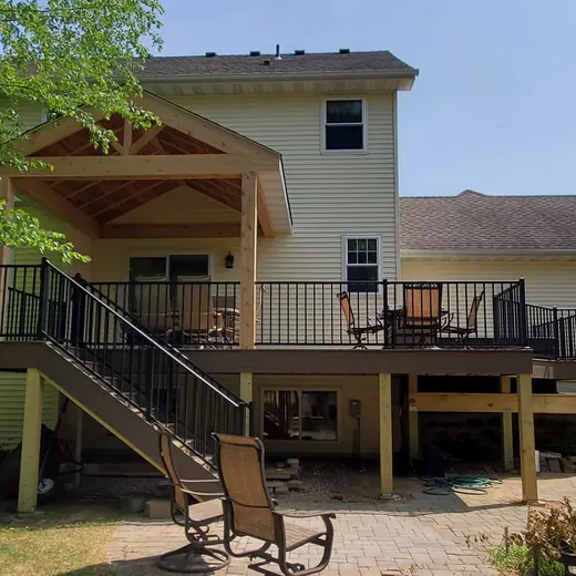 Backyard house with raised deck, stairs, and patio seating under a large tree