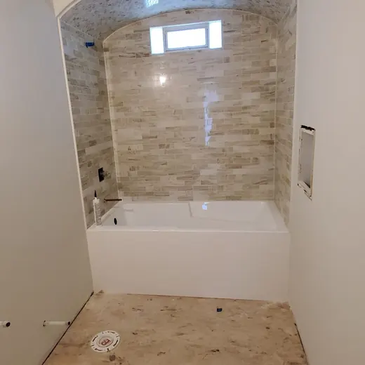 Bathroom under renovation with a tiled alcove bathtub and unfinished floor.