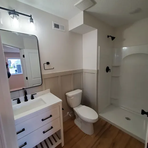 Bathroom with white vanity, toilet, and shower/tub combo, featuring beige walls and wood-look flooring