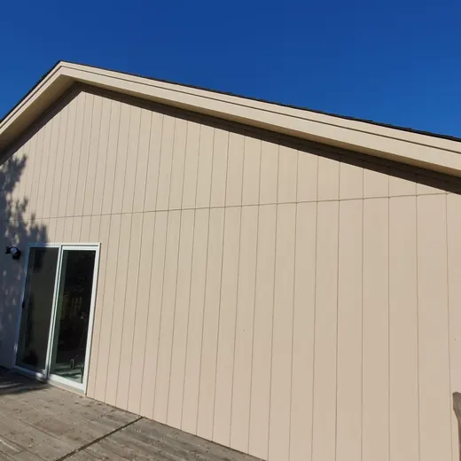 Beige house exterior with a sloped roof, sliding glass door, and clear blue sky.