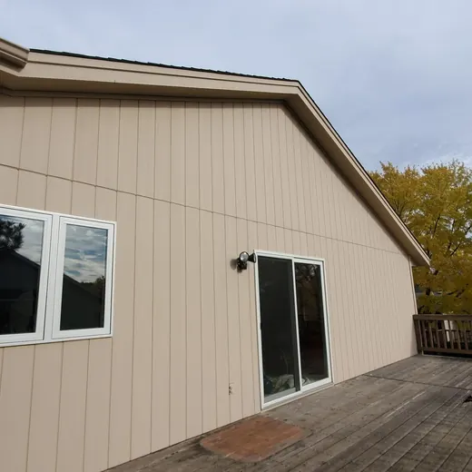 Beige house exterior with two windows and a deck beside autumn trees