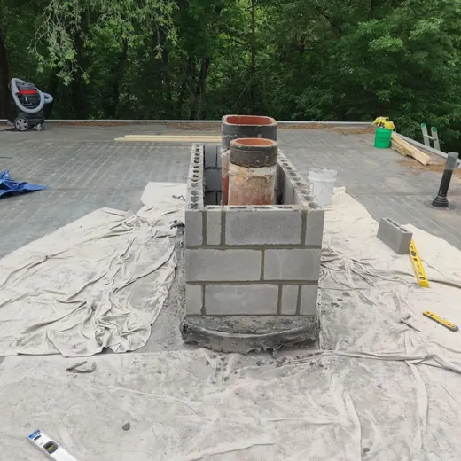Brick chimney under construction on a tarp-covered rooftop with tools nearby.