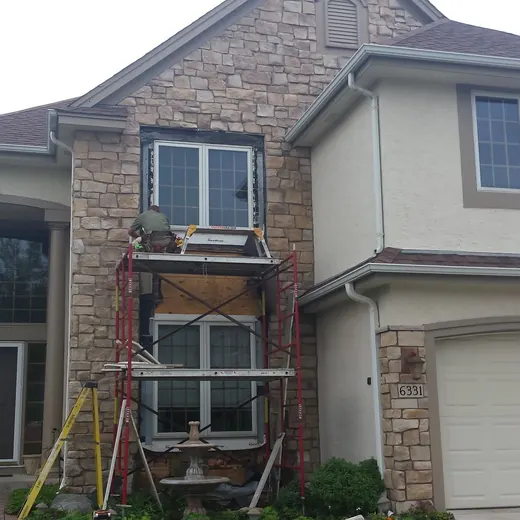Brick suburban house with front scaffolding and ladder, under repair beside a garage.