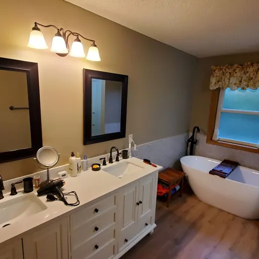 Bright bathroom with dual vanity, mirrors, and a freestanding tub by a window with a valance.