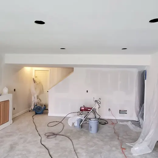 Bright living room renovation with white walls, exposed floor, and plastic-covered doorway