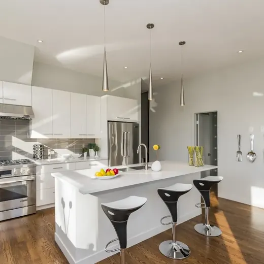Bright modern kitchen with white island, stools, stainless appliances, and wood floors