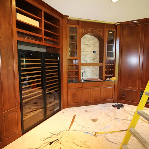 Built-in wine closet with wood cabinets and a person on a ladder working on the ceiling