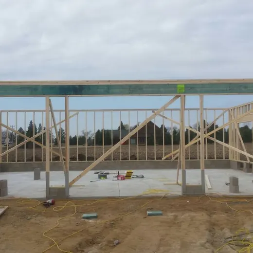 Construction site with concrete foundation, steel framing, and red scaffold supports under a partly built roof