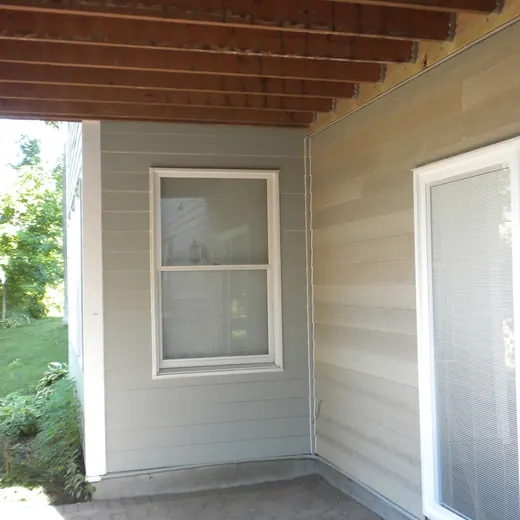 Covered porch with wood ceiling, gray siding, a window, and a white screen door.