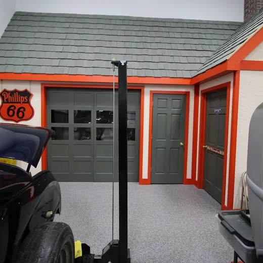 Custom Route 66 garage with gray door, orange trim, and vintage cars in the foreground