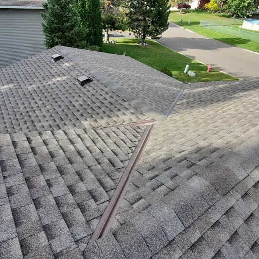 Damaged shingled roof with a visible ridge line and neighboring houses in the background