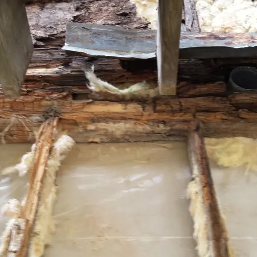Damaged wooden floor with exposed insulation, moisture stains, and a black pipe opening