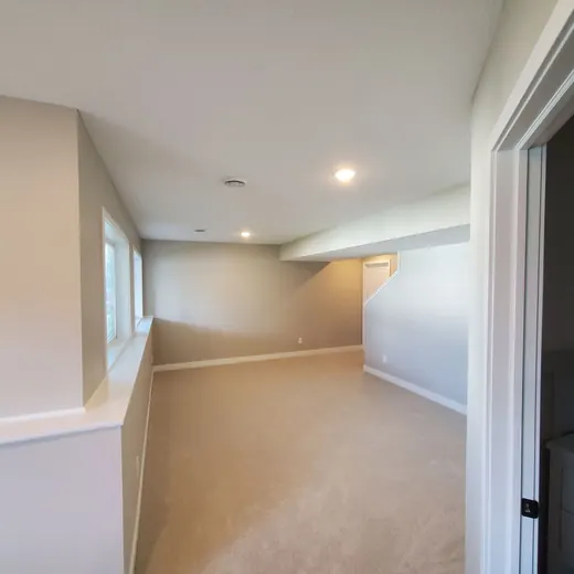 Empty beige carpeted room with recessed lights, white trim, and an open doorway on the right