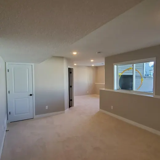 Empty beige hallway and living area with white doors, windows, and recessed ceiling lights