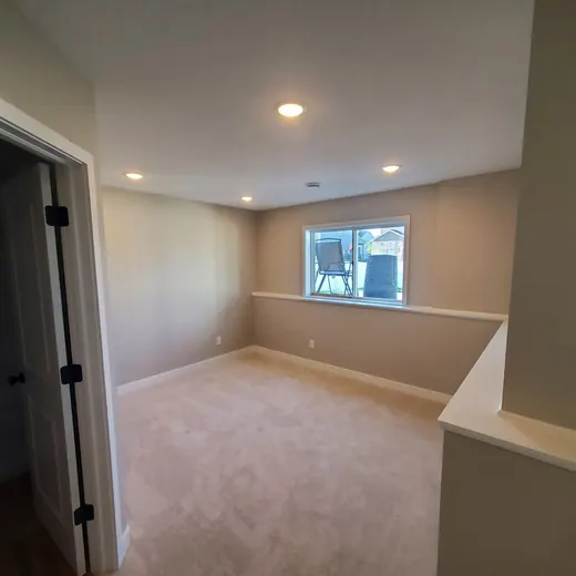Empty beige room with carpet, recessed lights, and a small window overlooking the street