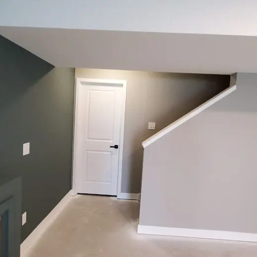 Empty gray room with stairs, white door, and small window ledge.