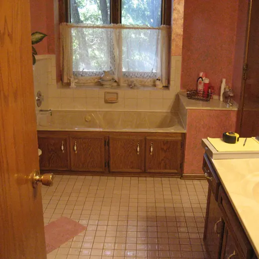 Empty kitchen with tan tile floor, wood cabinets, and a sink beneath a window.