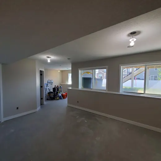 Empty living room with carpet, beige walls, recessed lights, and large windows overlooking a yard