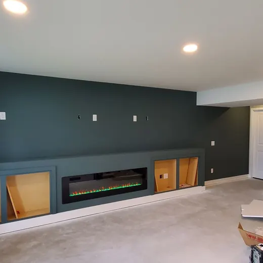 Empty living room with dark green accent wall, fireplace, windows, and a stairway to the right