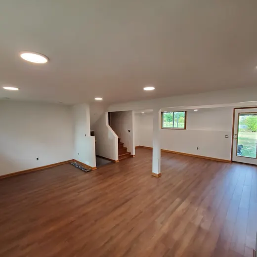 Empty open-plan living room with wood floors, white walls, recessed lights, and sliding glass door to outside