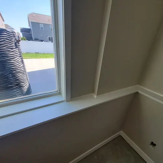 Empty room corner with a large window, beige walls, and white trim overlooking a driveway and street.
