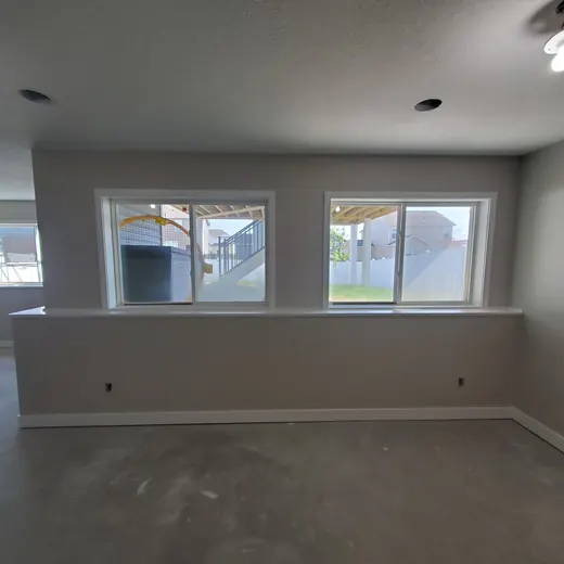 Empty unfinished living room with gray carpet, white walls, recessed lights, and large windows overlooking a backyard