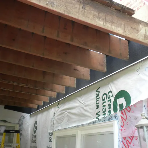 Exposed wooden ceiling joists above wrapped wall sheathing and a window opening in a construction area