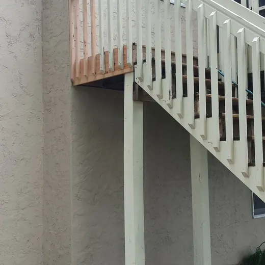 Exterior staircase with white railing beside a beige stucco building and paint cans on the ground.