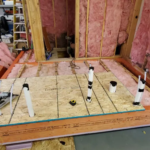 Framed basement floor with exposed insulation, plumbing pipes, and orange lumber around the perimeter