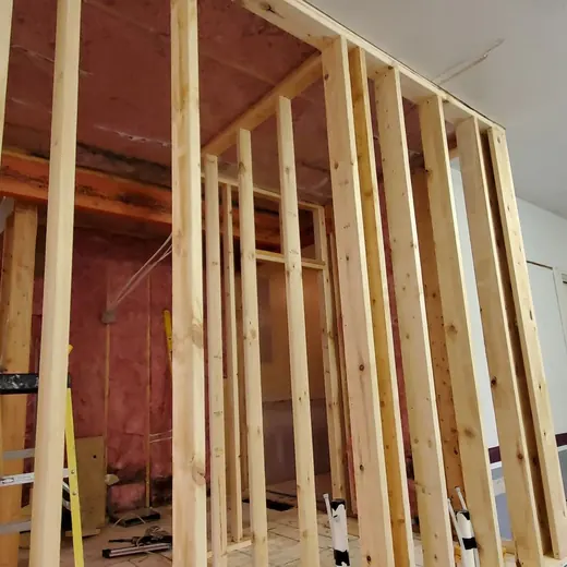 Framed interior wall under construction in a garage, with exposed wood studs and a step ladder nearby