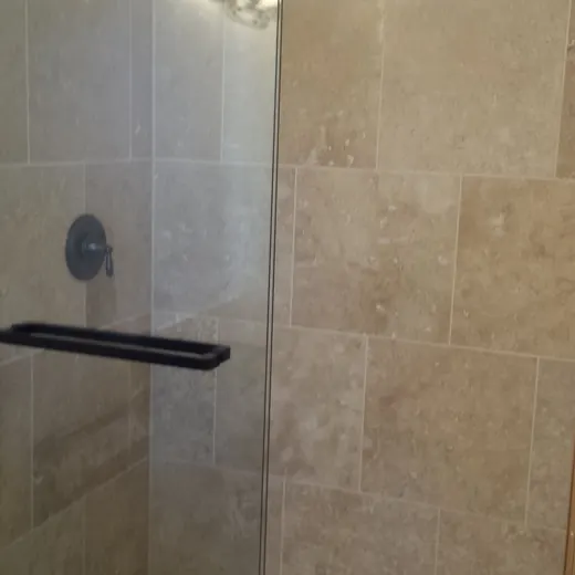 Glass shower with beige tile walls, black grab bar, and mosaic tile floor.