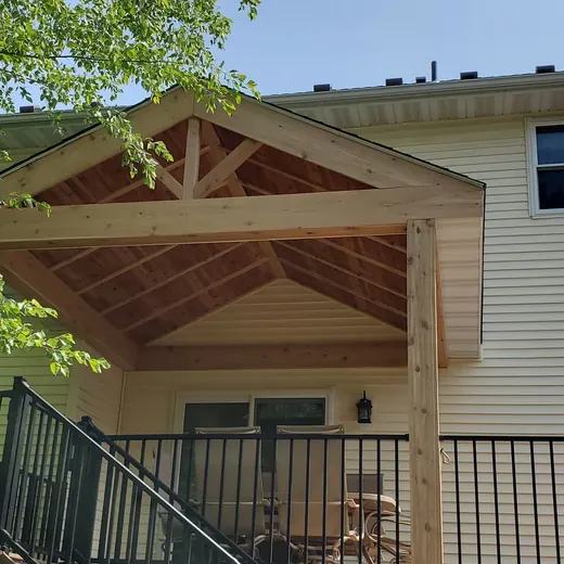 House with a covered porch, wooden truss roof, and black metal railing in bright daylight