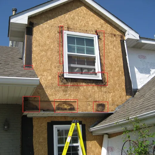 House exterior with a ladder leaning against a small upper window and red trim markings around the facade