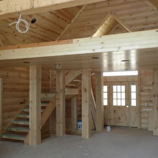 Interior of a unfinished wooden house with exposed beams, staircase, and loft area