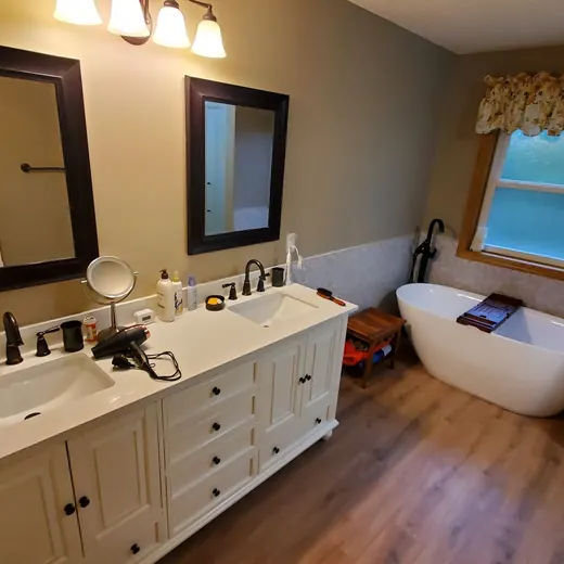 Modern bathroom with double vanity, mirror, freestanding tub, and wood-look floor.