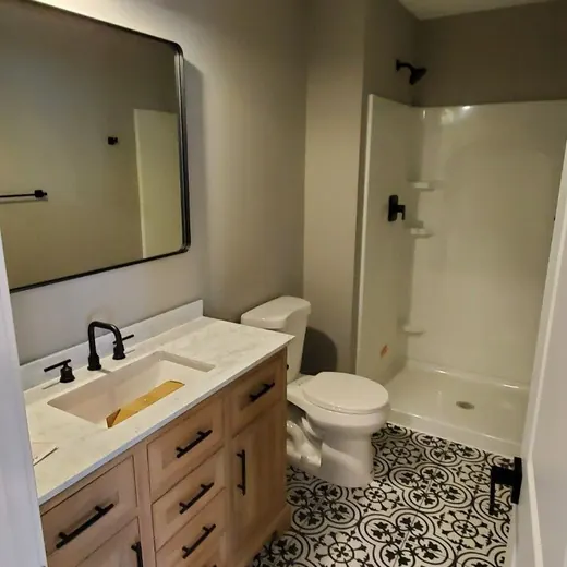 Modern bathroom with wood vanity, black mirror light, white toilet, and patterned black-and-white floor tile