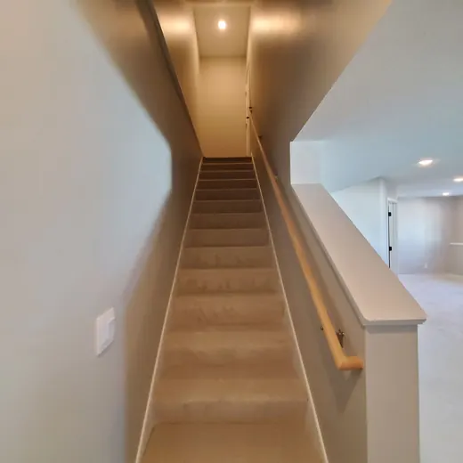Narrow carpeted staircase in a beige interior hallway with white walls and a wooden handrail