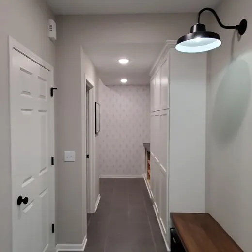 Narrow hallway with gray tile floor, white walls, ceiling light, and a wooden bench along the right wall.
