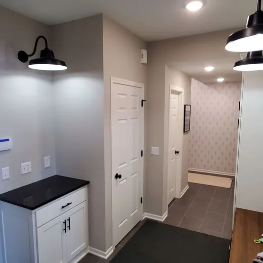 Narrow hallway with white doors, gray walls, black sconces, and a small cabinet