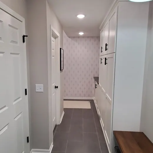 Narrow hallway with white doors, recessed lights, and a dark floor runner leading to a room.
