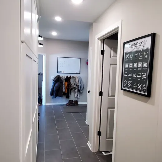 Narrow hallway with white walls, gray carpet, recessed lights, and a doorway with a wall sign on the right.