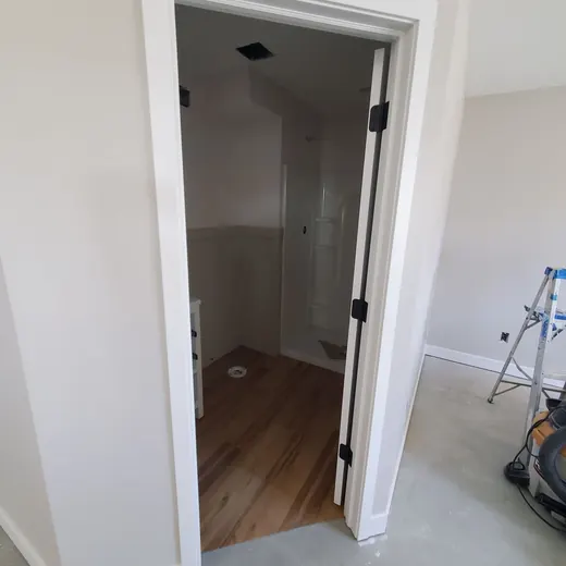 Open doorway to a small closet or hallway with wood floor, white trim, and unfinished room walls
