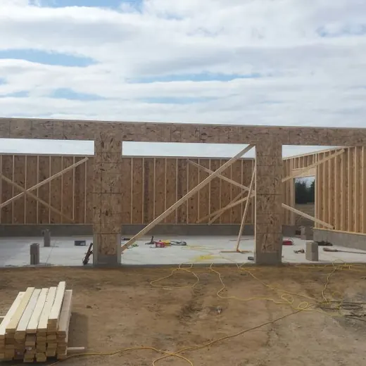 Partially built wooden house framing at a construction site with ladders and lumber on the ground