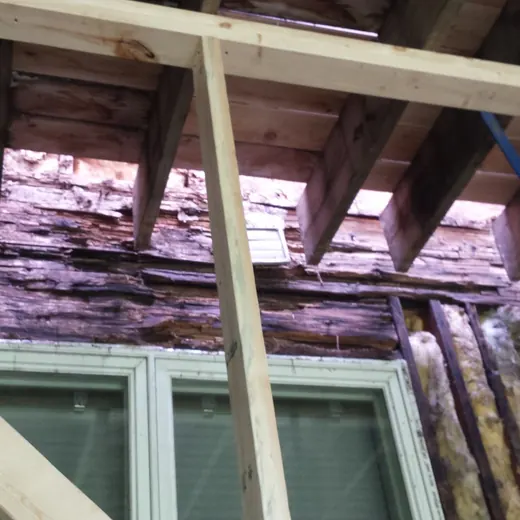 Partially demolished roof above a window, exposing damaged wood framing and insulation.