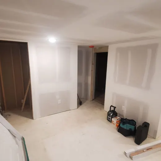 Partially finished room with drywall, a dark door, ceiling light, and tools on the floor.