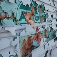 Peeling white exterior paint with exposed teal and rust-colored layers on a weathered wall