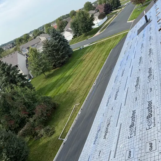 Roof with underlayment beside a suburban street and grassy yard on a clear day